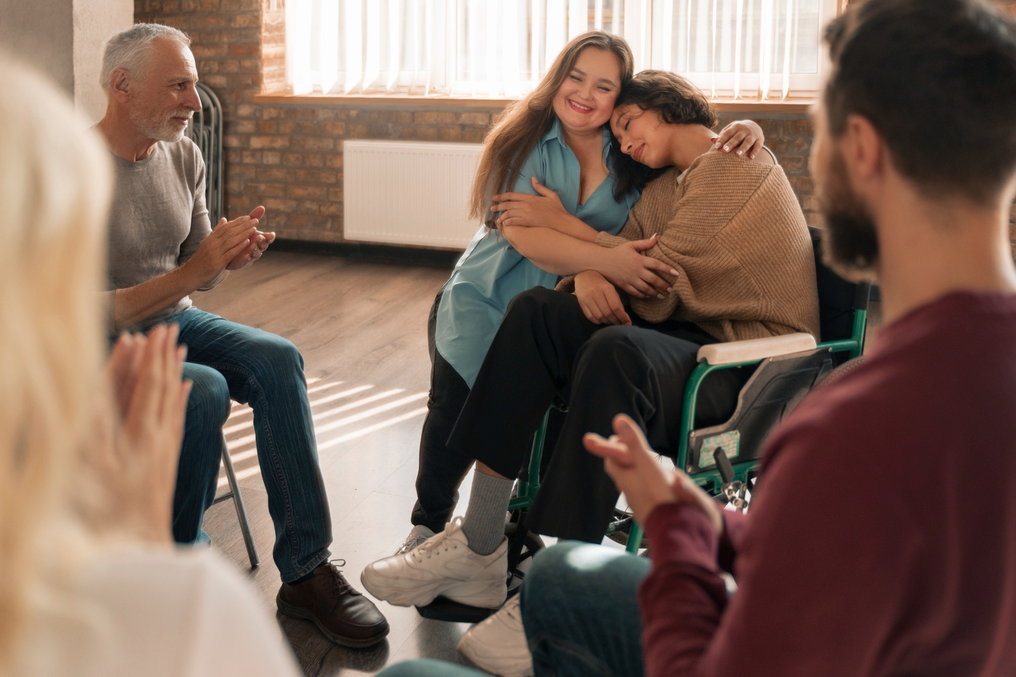 Two women embracing while participants applaud during a DBT therapy group session in Mount Pleasant, WI.