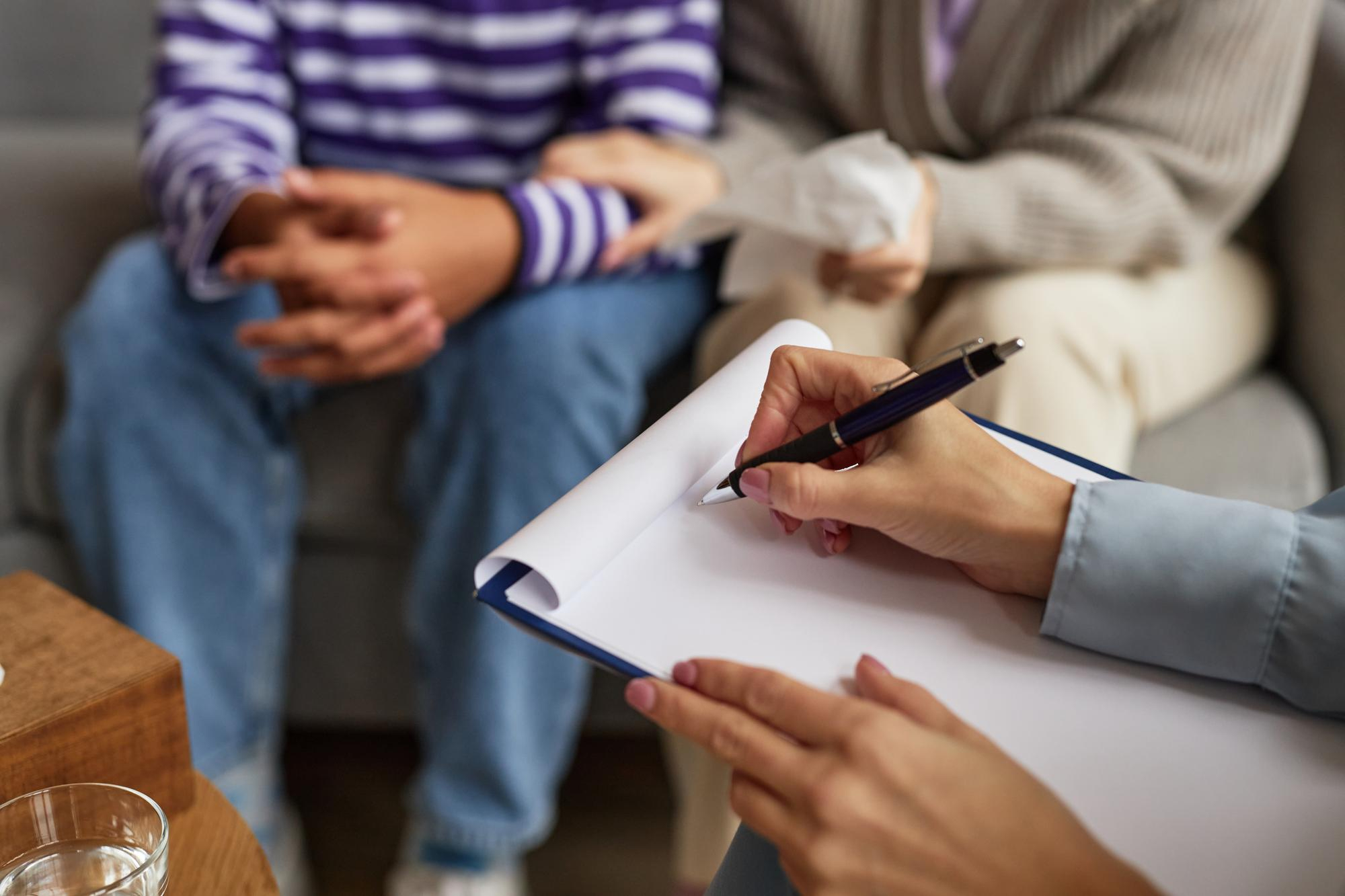 Therapist taking notes while a couple holds hands during PTSD treatment in Mount Pleasant, WI.
