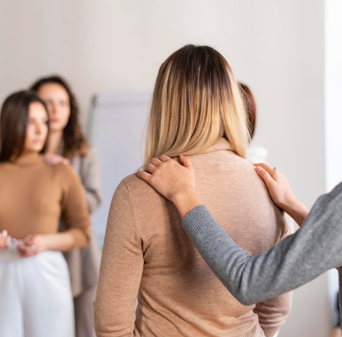 Two women comforting each other while looking in a mirror during a therapy session in Mount Pleasant, WI.