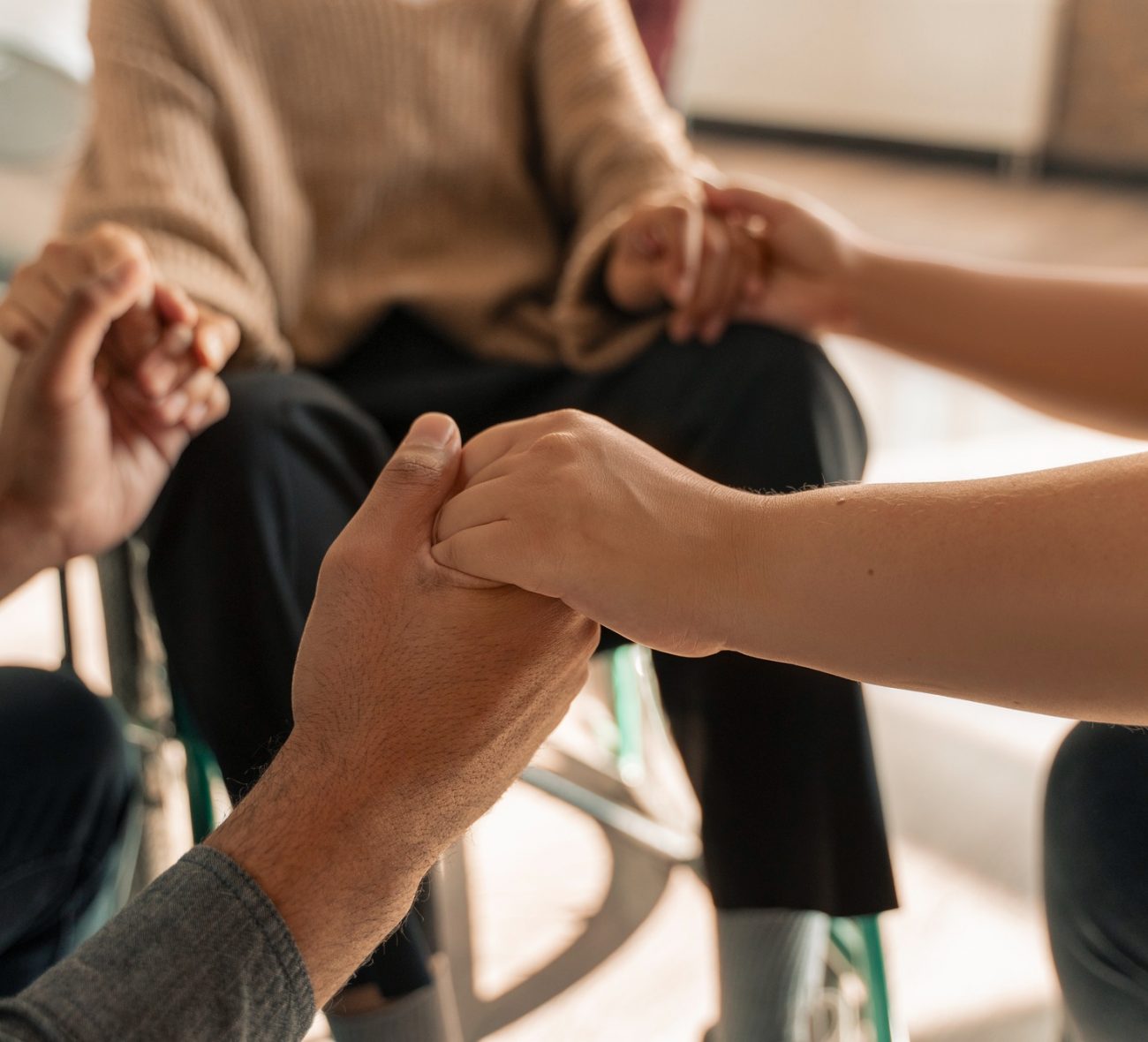 Three people holding hands in a therapy circle during addiction treatment in Mount Pleasant, WI.