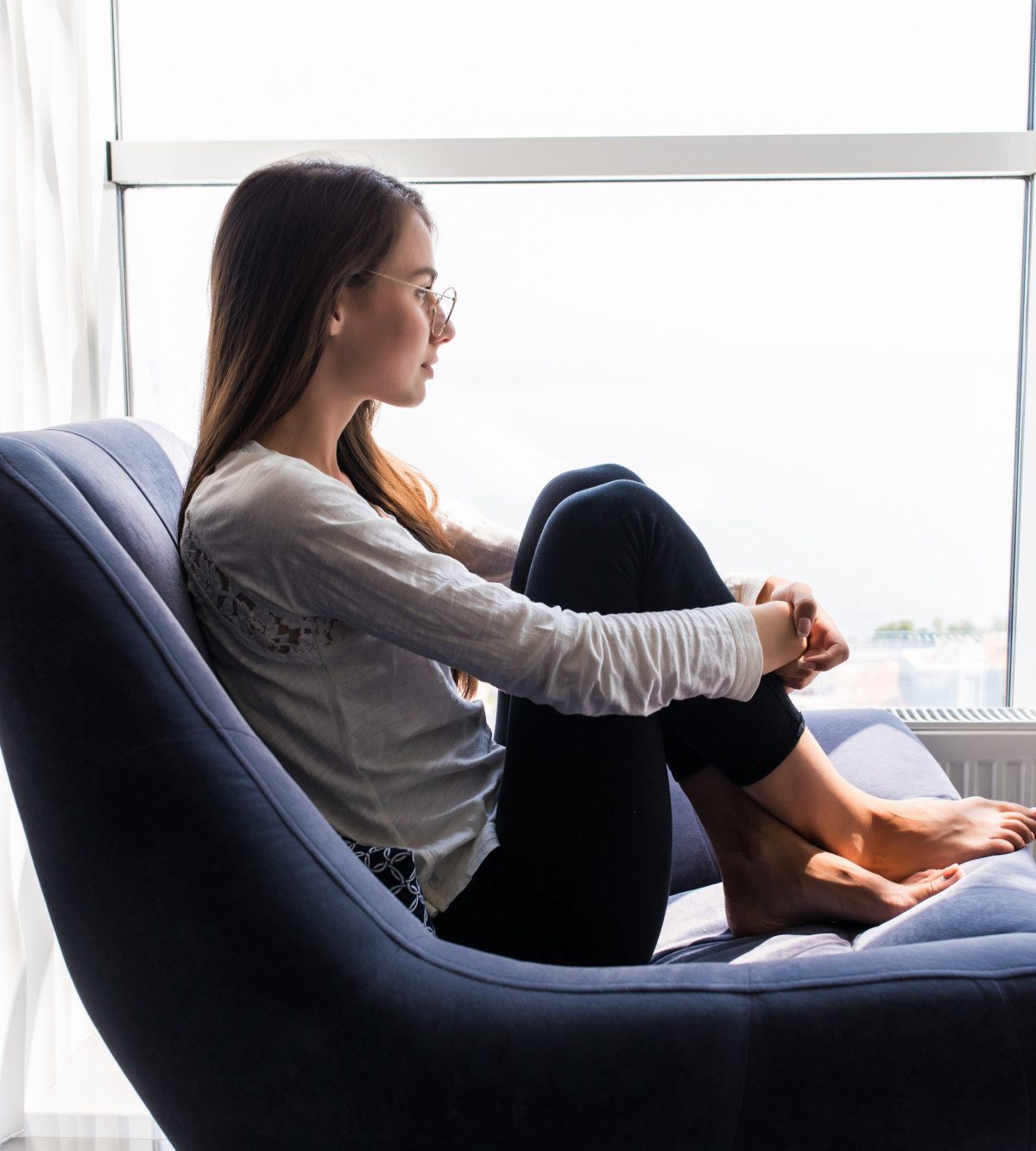 Woman sitting in a chair and enjoying sunlight through a window during her recovery journey.